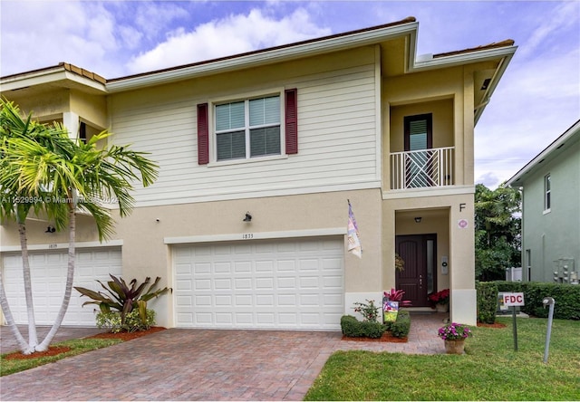 townhome / multi-family property with a garage, a balcony, decorative driveway, and stucco siding