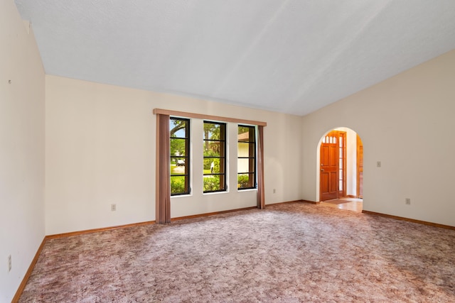 carpeted empty room with lofted ceiling, baseboards, and arched walkways