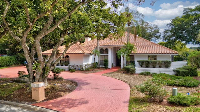 mediterranean / spanish-style home with a tile roof, a chimney, decorative driveway, and stucco siding