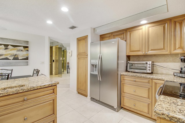 kitchen with light tile patterned floors, light stone counters, a toaster, visible vents, and stainless steel refrigerator with ice dispenser