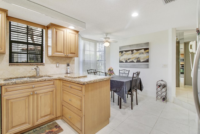 kitchen with light stone counters, light tile patterned flooring, a peninsula, a sink, and backsplash