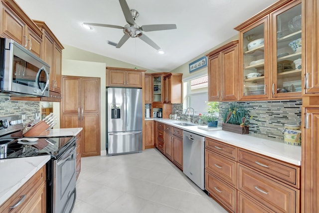 kitchen with vaulted ceiling, appliances with stainless steel finishes, brown cabinetry, and a sink