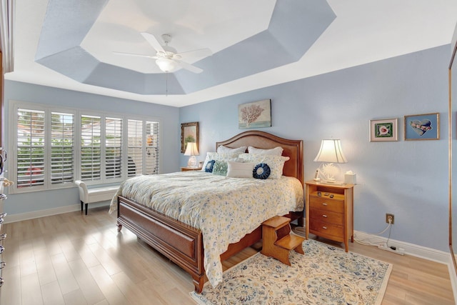 bedroom with a tray ceiling, a ceiling fan, light wood-style flooring, and baseboards