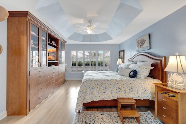 bedroom with light wood-type flooring, baseboards, a tray ceiling, and ceiling fan