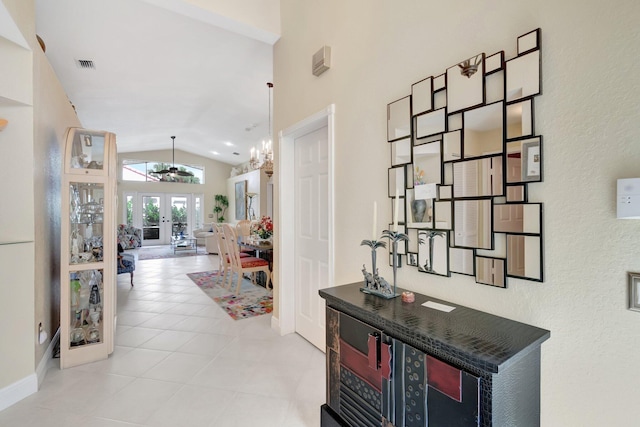 hallway featuring lofted ceiling, light tile patterned floors, visible vents, and french doors