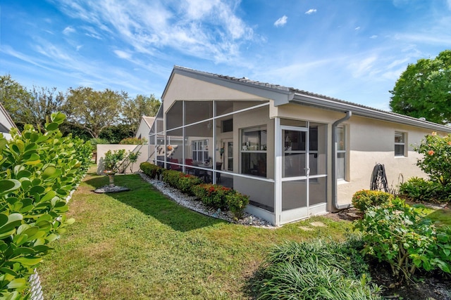 back of property featuring a sunroom, stucco siding, a yard, and fence