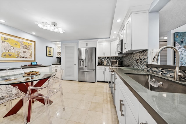 kitchen featuring dark countertops, a sink, stainless steel appliances, white cabinetry, and backsplash