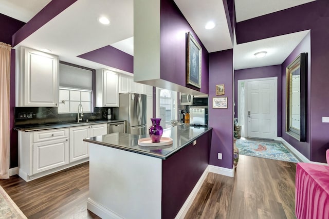 kitchen with stainless steel appliances, dark wood-type flooring, a peninsula, a sink, and dark countertops