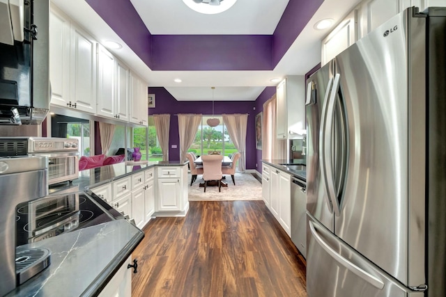 kitchen featuring dark wood finished floors, white cabinets, appliances with stainless steel finishes, dark countertops, and a raised ceiling