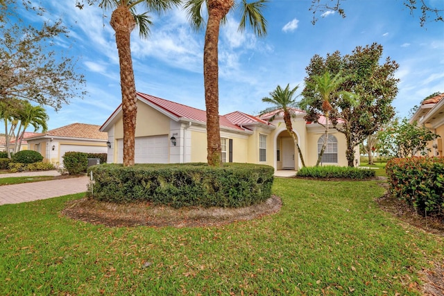 mediterranean / spanish-style home featuring stucco siding, an attached garage, a front yard, metal roof, and driveway