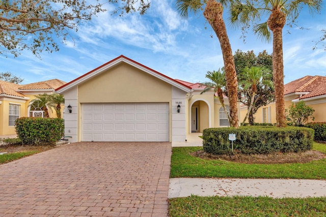 mediterranean / spanish home with an attached garage, a tile roof, decorative driveway, and stucco siding