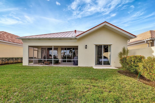 back of house featuring metal roof, a sunroom, a lawn, stucco siding, and a standing seam roof