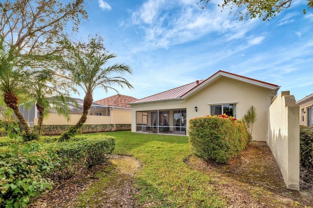 rear view of property with a lawn, a sunroom, metal roof, fence, and stucco siding