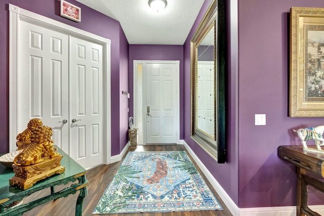 doorway to outside featuring baseboards, dark wood-type flooring, and a textured ceiling