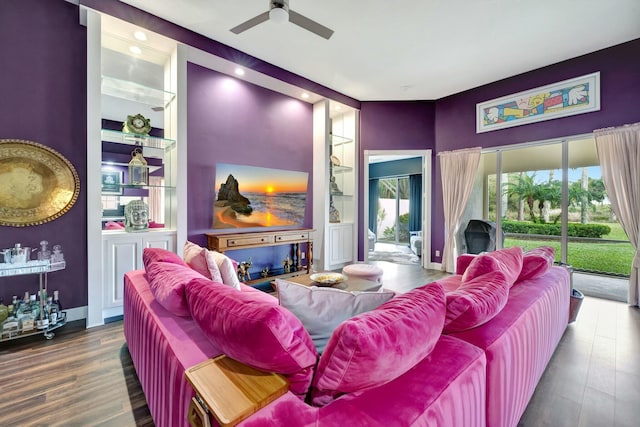 cinema room featuring a ceiling fan, built in shelves, baseboards, and wood finished floors