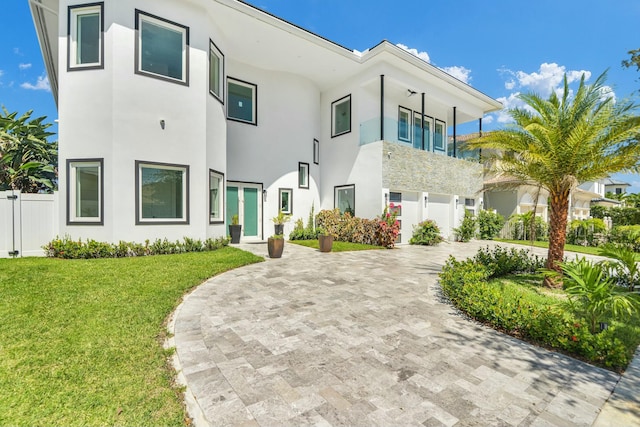 view of front of property featuring decorative driveway, fence, a front lawn, and stucco siding