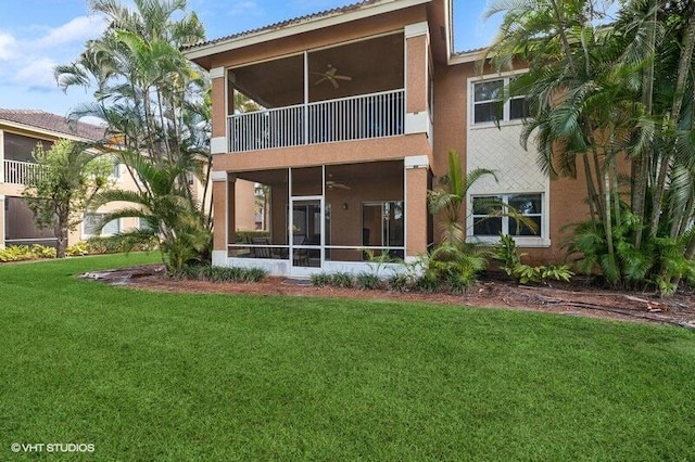 rear view of house with stucco siding, a lawn, a ceiling fan, a sunroom, and a balcony