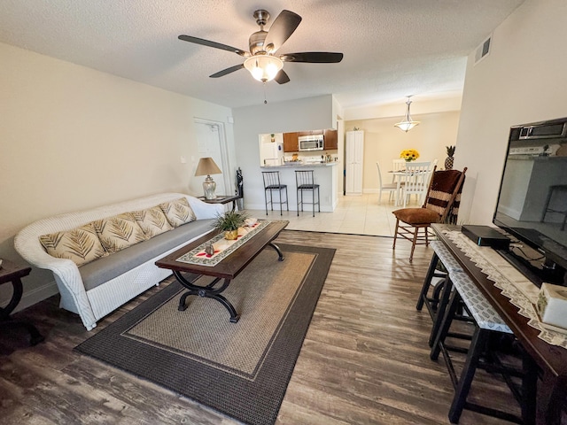 living room featuring baseboards, visible vents, a ceiling fan, wood finished floors, and a textured ceiling