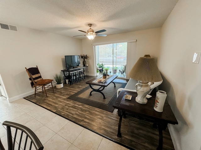 living room with baseboards, visible vents, a ceiling fan, wood finished floors, and a textured ceiling