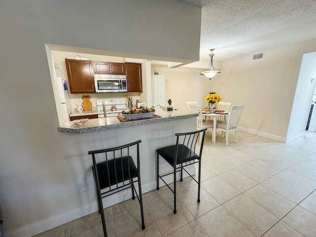 kitchen with white range with electric stovetop, stainless steel microwave, a breakfast bar area, a peninsula, and a textured ceiling