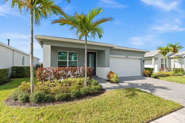 ranch-style home with a garage, a front yard, decorative driveway, and stucco siding