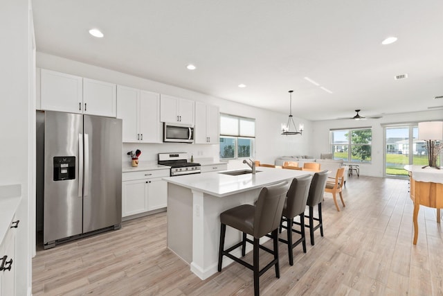 kitchen featuring light wood finished floors, white cabinets, open floor plan, stainless steel appliances, and a sink