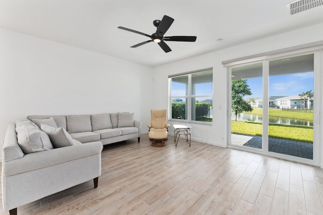 living area featuring a water view, a ceiling fan, visible vents, baseboards, and light wood finished floors