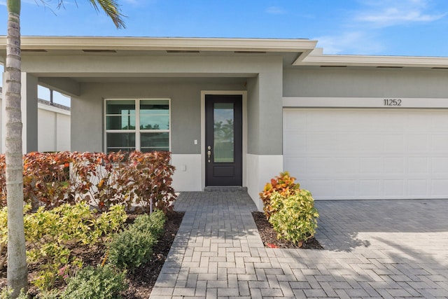 view of exterior entry featuring a garage, decorative driveway, and stucco siding