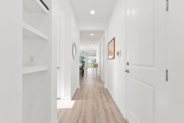 hall featuring baseboards, light wood-style flooring, and recessed lighting