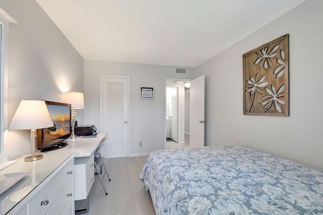 bedroom with light wood finished floors, baseboards, visible vents, and a closet