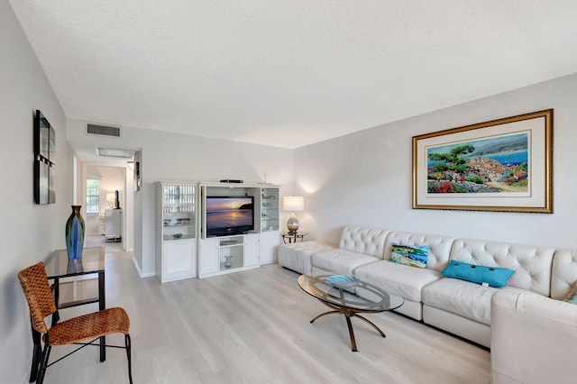 living area featuring light wood-type flooring, visible vents, and a textured ceiling