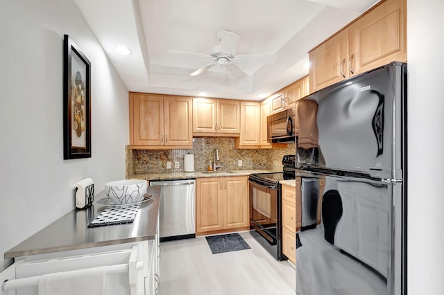 kitchen with a raised ceiling, backsplash, light brown cabinets, a sink, and black appliances