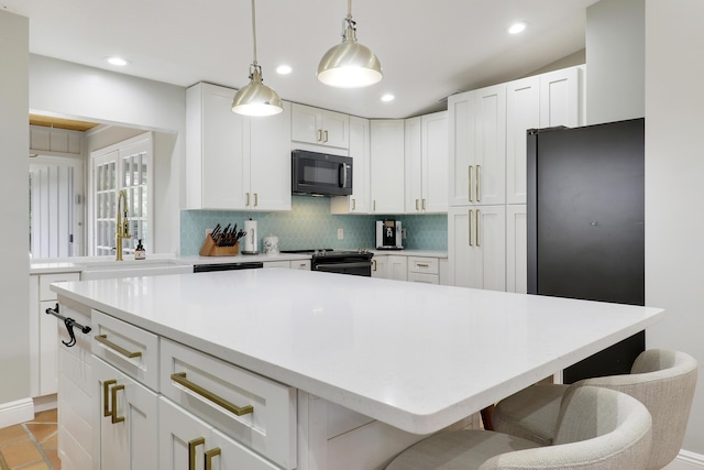 kitchen featuring a breakfast bar, a sink, white cabinetry, backsplash, and black appliances