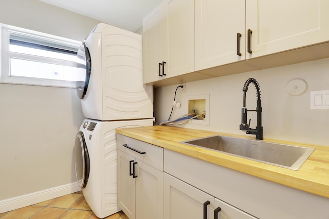 laundry room featuring light tile patterned floors, stacked washer / dryer, a sink, baseboards, and cabinet space