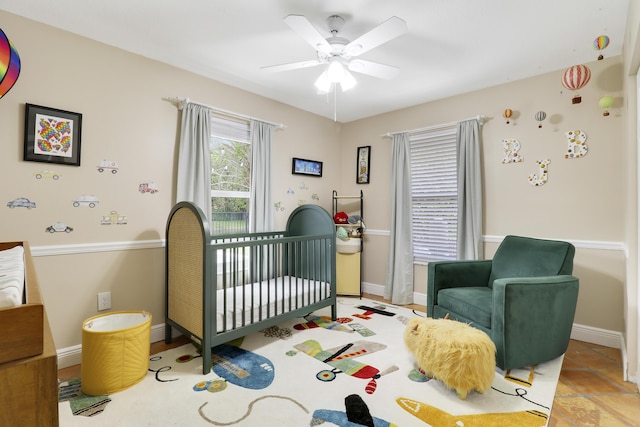 bedroom featuring ceiling fan, a crib, and baseboards