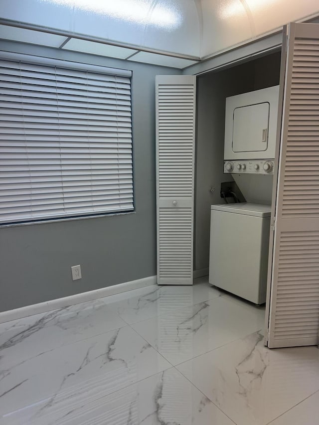 laundry room featuring laundry area, baseboards, marble finish floor, and stacked washer and clothes dryer