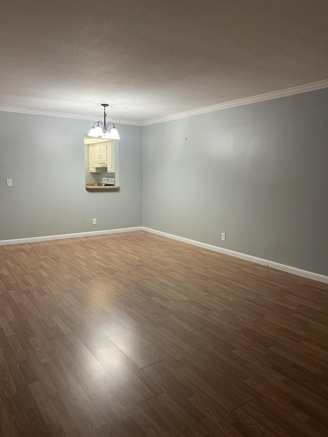 spare room featuring an inviting chandelier, baseboards, dark wood finished floors, and crown molding