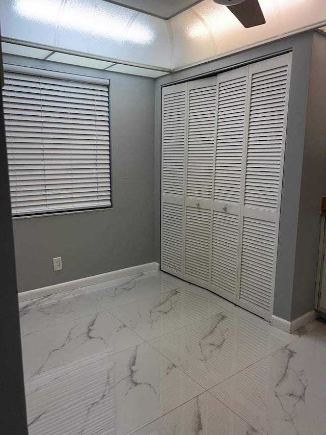 unfurnished bedroom with ceiling fan, marble finish floor, a closet, and baseboards