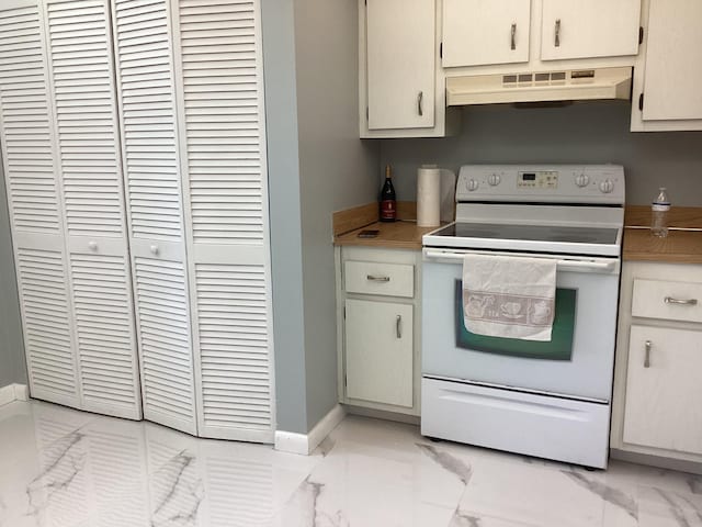 kitchen featuring white electric stove, baseboards, marble finish floor, light countertops, and under cabinet range hood