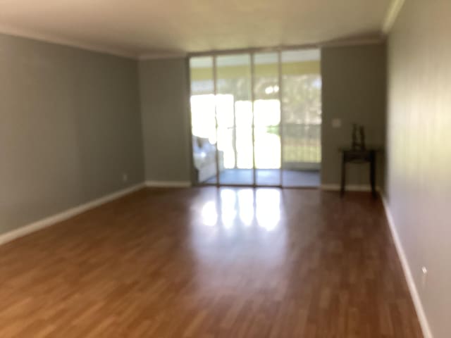 empty room with baseboards, wood finished floors, and crown molding