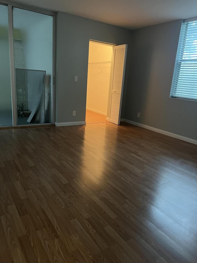 unfurnished bedroom featuring dark wood-style floors, a walk in closet, and baseboards