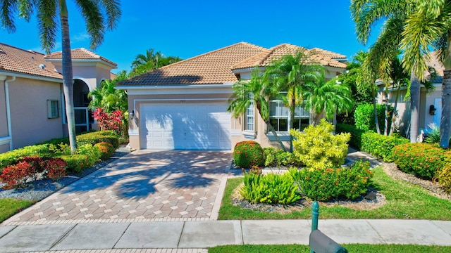 mediterranean / spanish house with an attached garage, a tiled roof, decorative driveway, and stucco siding