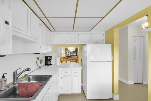 kitchen featuring light tile patterned flooring, white appliances, a sink, white cabinetry, and light countertops