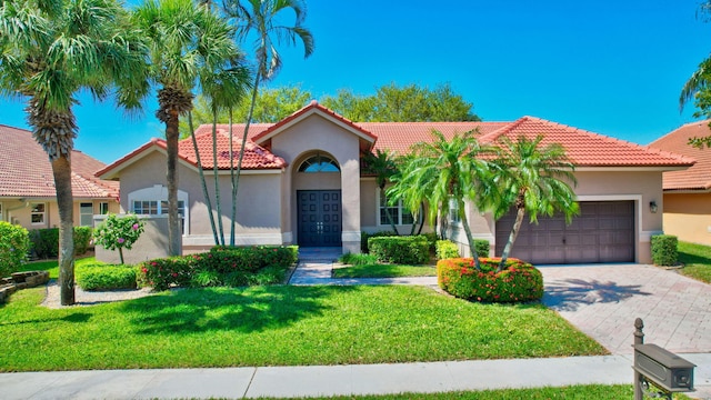 mediterranean / spanish home featuring decorative driveway, a tile roof, stucco siding, an attached garage, and a front yard