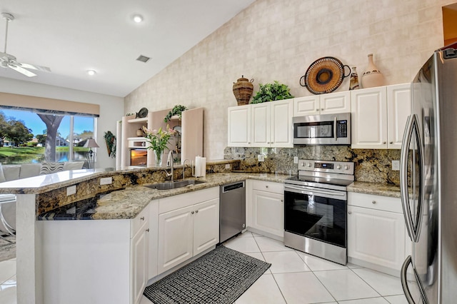 kitchen with light tile patterned floors, appliances with stainless steel finishes, vaulted ceiling, a sink, and a peninsula