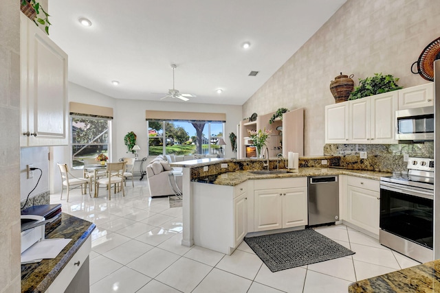 kitchen featuring light stone counters, stainless steel appliances, open floor plan, a sink, and a peninsula