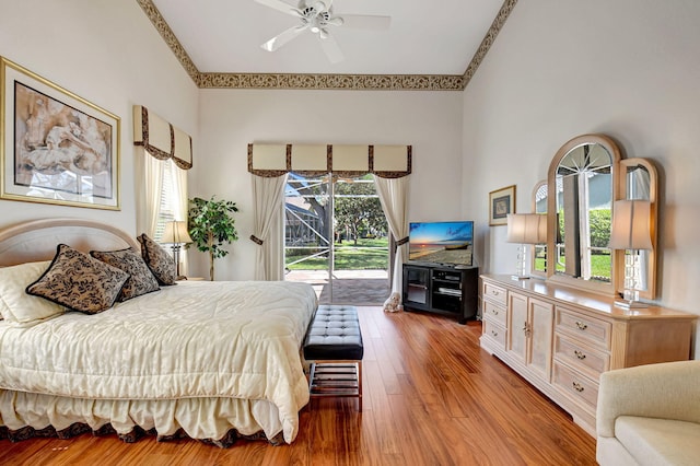 bedroom featuring access to outside, a high ceiling, a ceiling fan, and wood finished floors