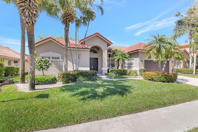 mediterranean / spanish-style home with a garage, a tiled roof, a front lawn, and stucco siding