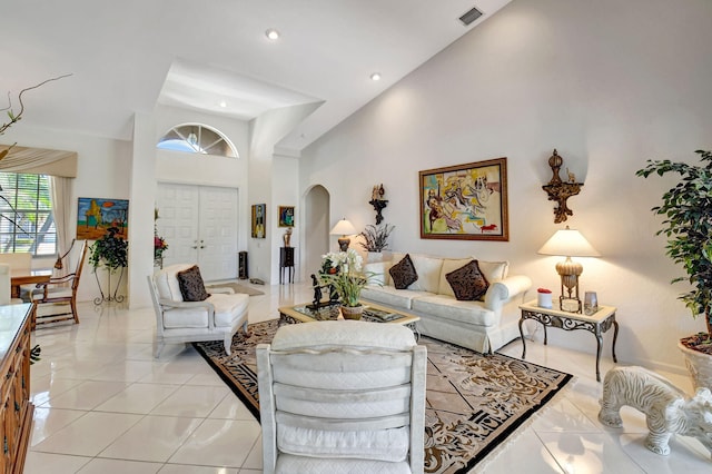 living area with light tile patterned floors, visible vents, arched walkways, a high ceiling, and recessed lighting