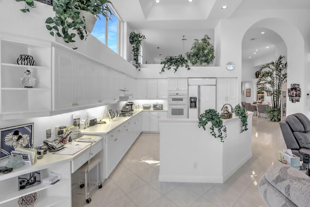 kitchen with white double oven, a towering ceiling, arched walkways, white cabinets, and paneled refrigerator